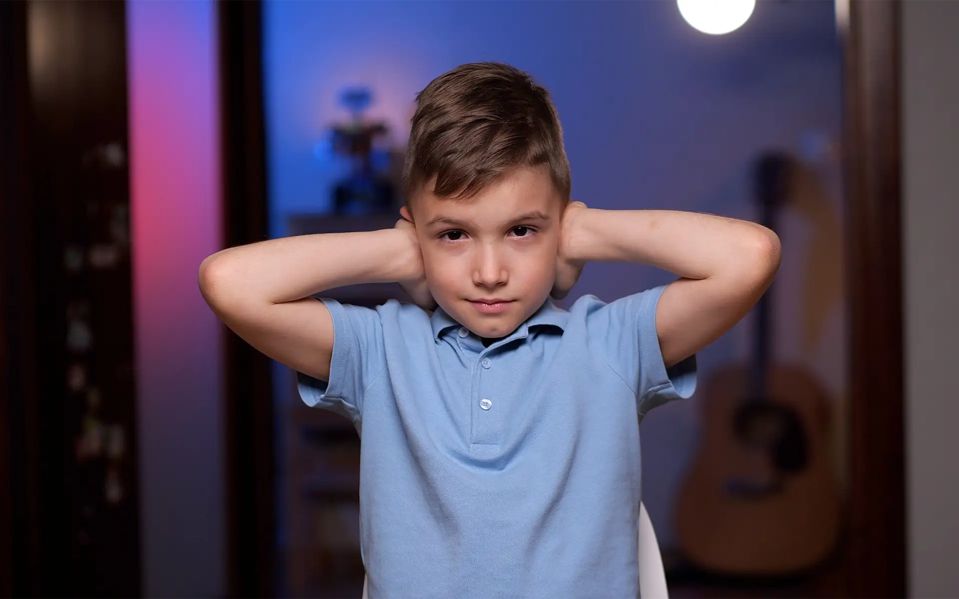 A young boy with a sensitivity to noise covering his ears with his hands