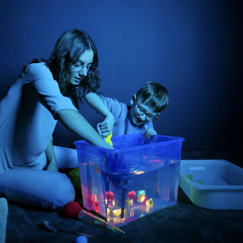 a woman playing a water sensory game with a child in a room with muted lighting