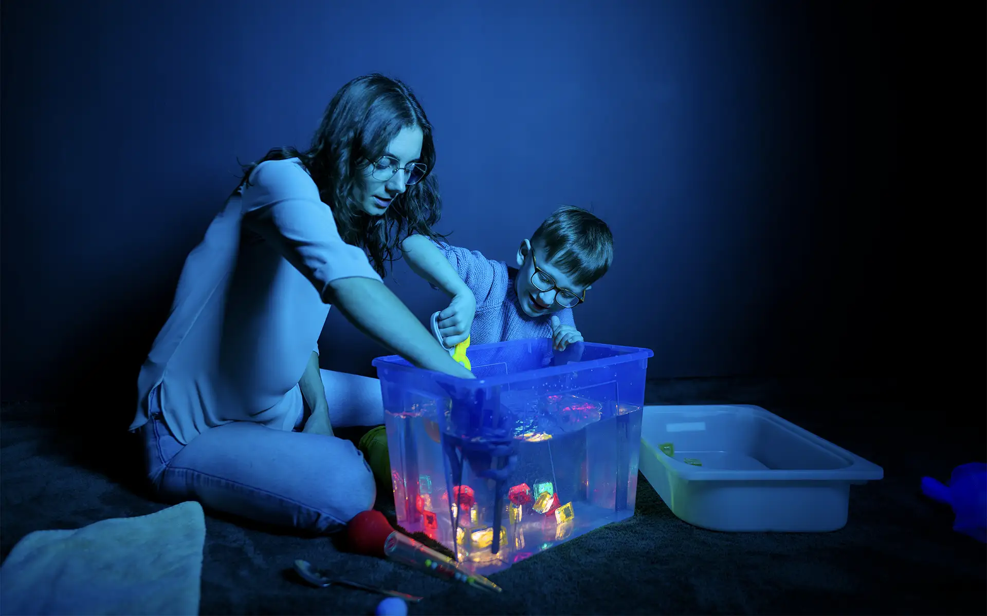 a woman playing a water sensory game with a child in a room with muted lighting