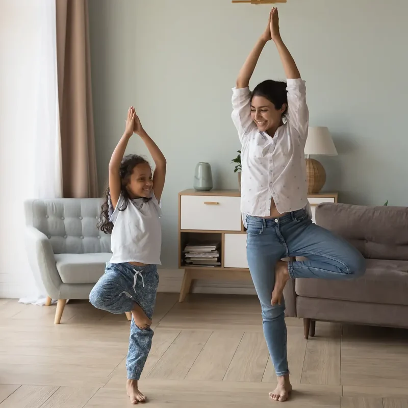 Woman and girl standing together in a tree pose in a living room