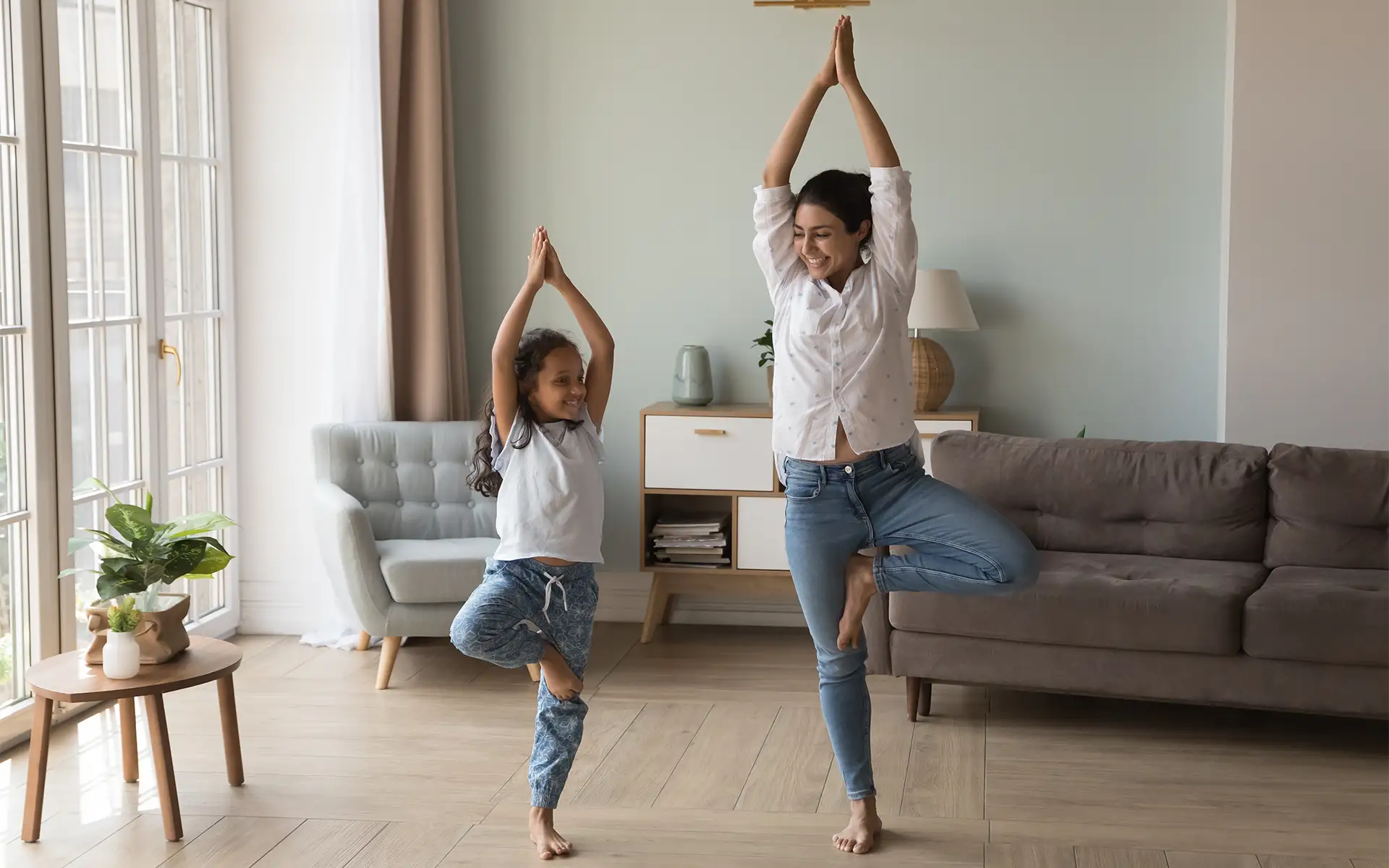 Woman and girl standing together in a tree pose in a living room