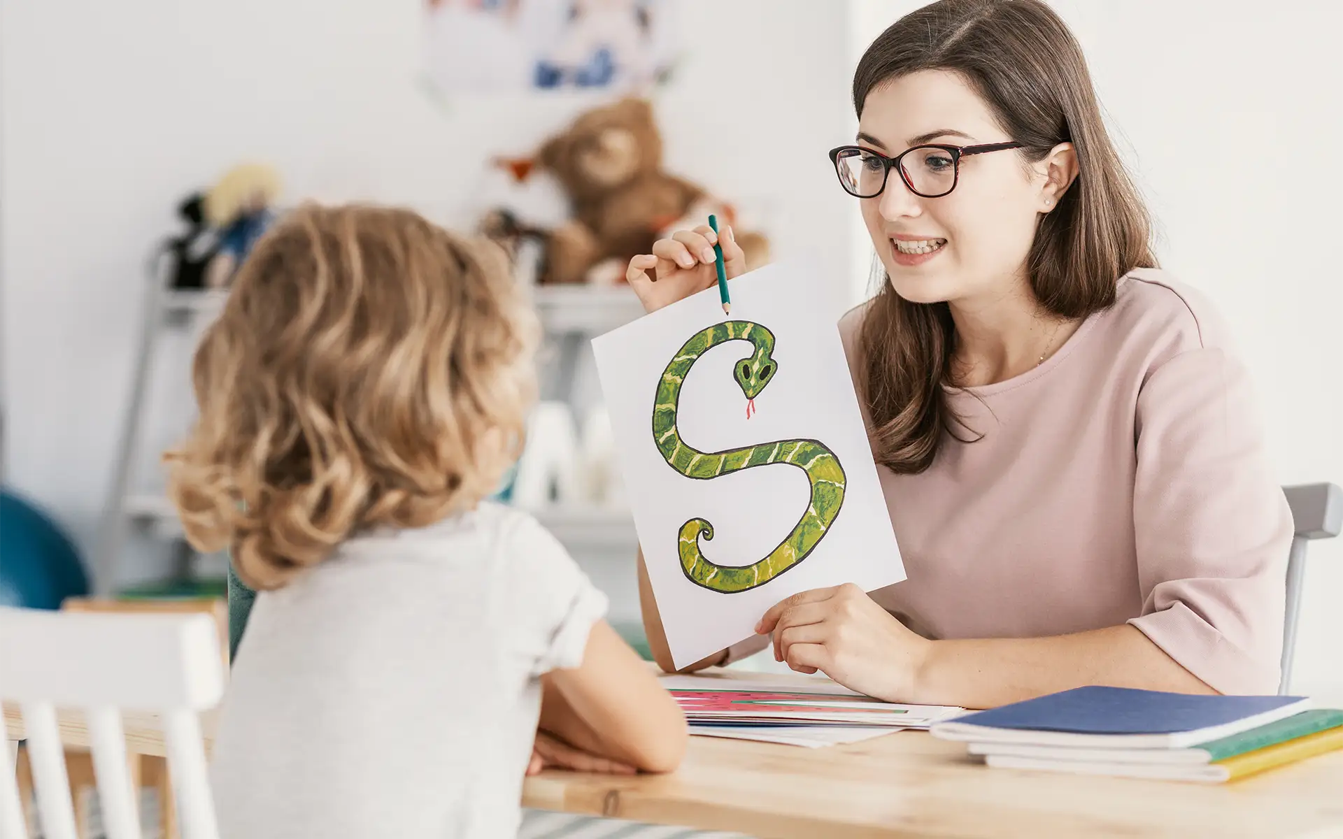 A female speech and language therapist holding a picture of a snake shaped like an "S" working with a young girl