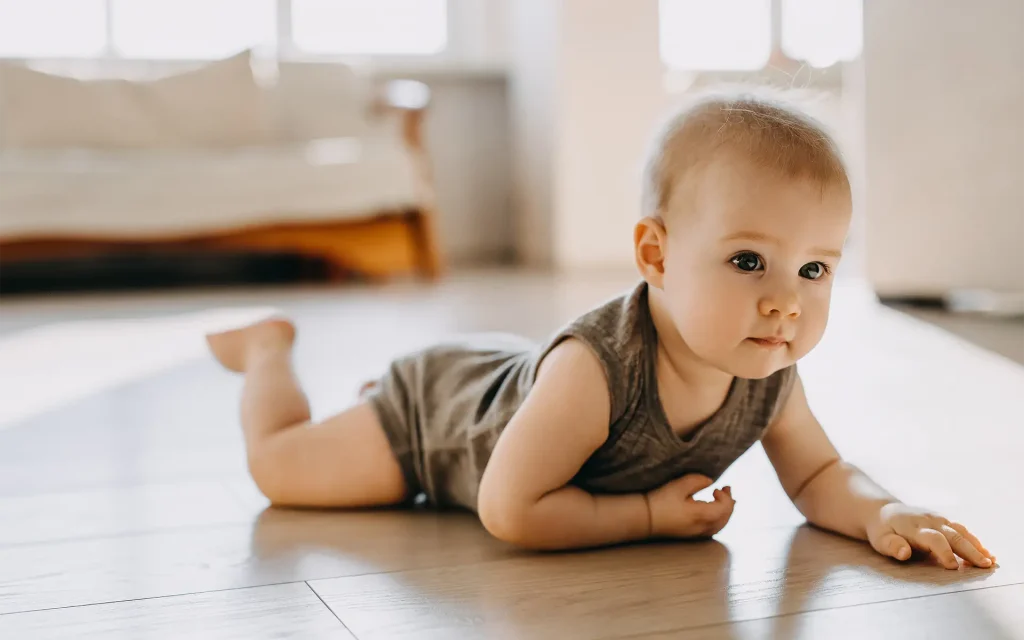 Baby on a wooden floor in a brown onesie, lying on its belly while looking up