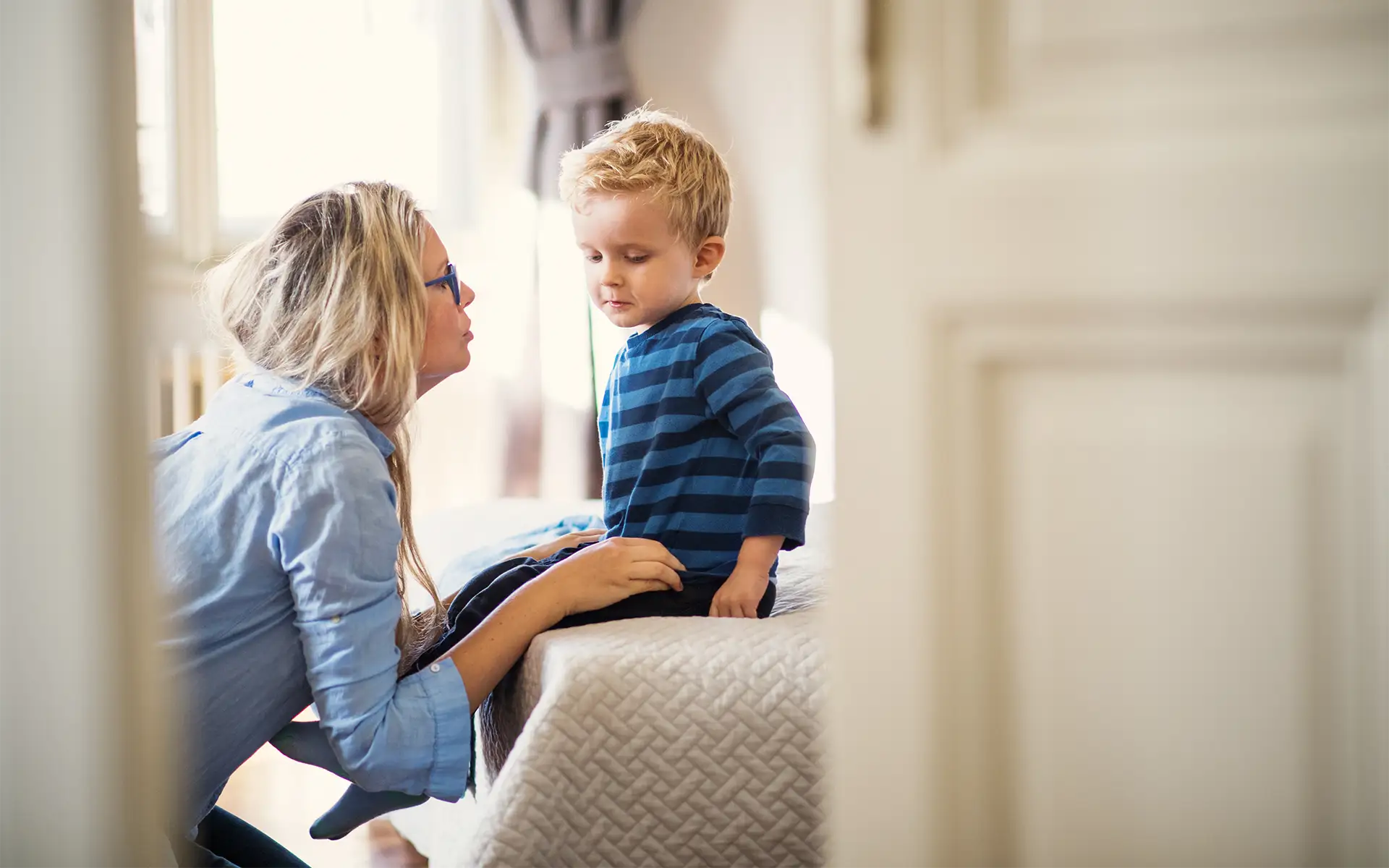 A young mother talking to her toddler son inside a bedroom