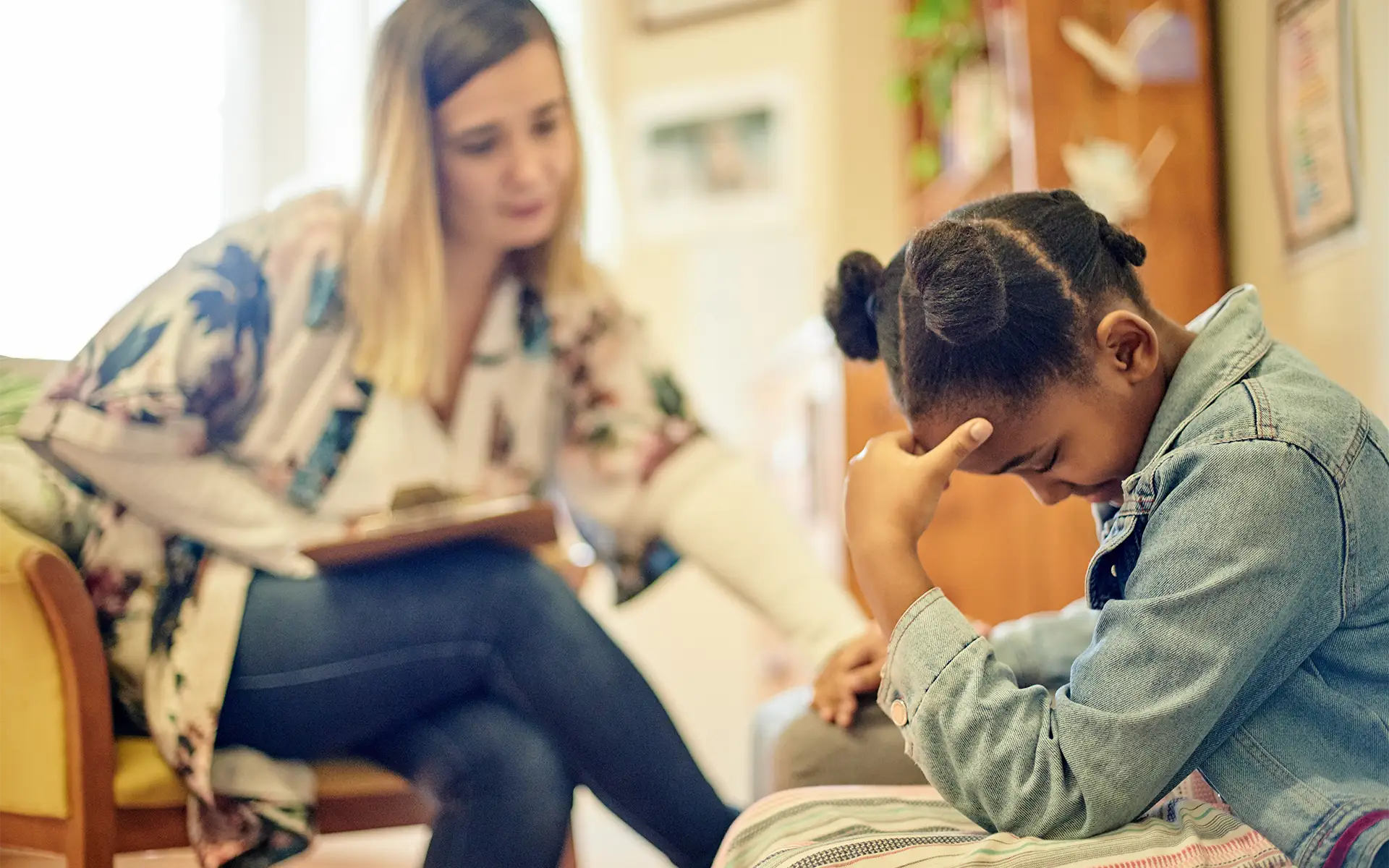 A sad young girl holds her head in her hand while sitting next to a counselor or therapist