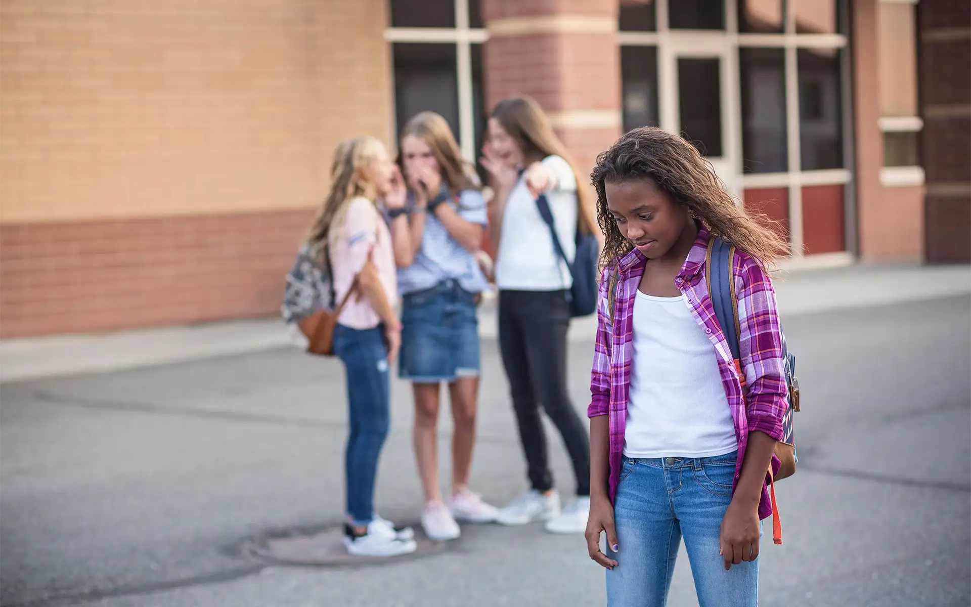 One young girl is being bullied and talked about behind her back by other students as she walks by