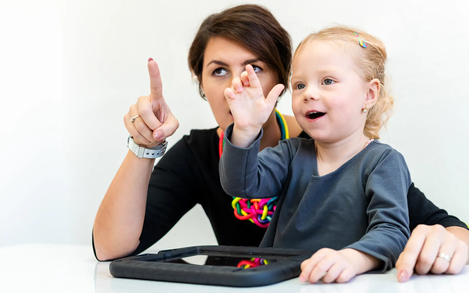A toddler girl sits next to a pediatric occupational therapist doing sensory exercises
