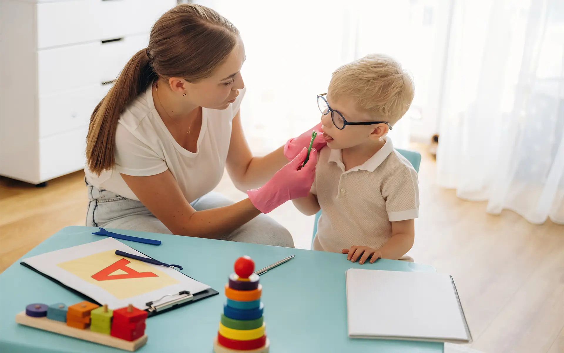 A female speech therapist working with a young boy using a special device on the tongue