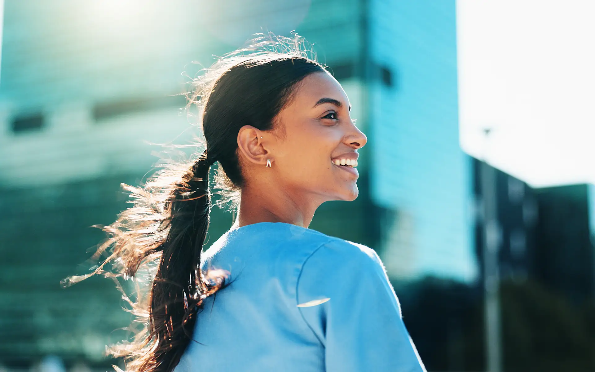 A smiling nurse in profile outside an office building with her ponytail blowing in the breeze