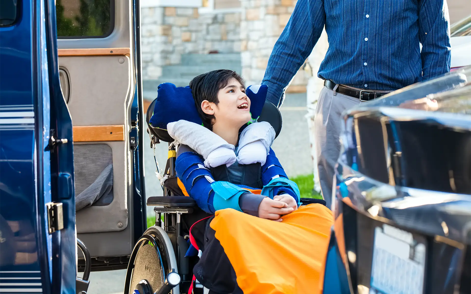 A father helps his son, who sits in a wheelchair, prepare to get into a van via a wheelchair lift