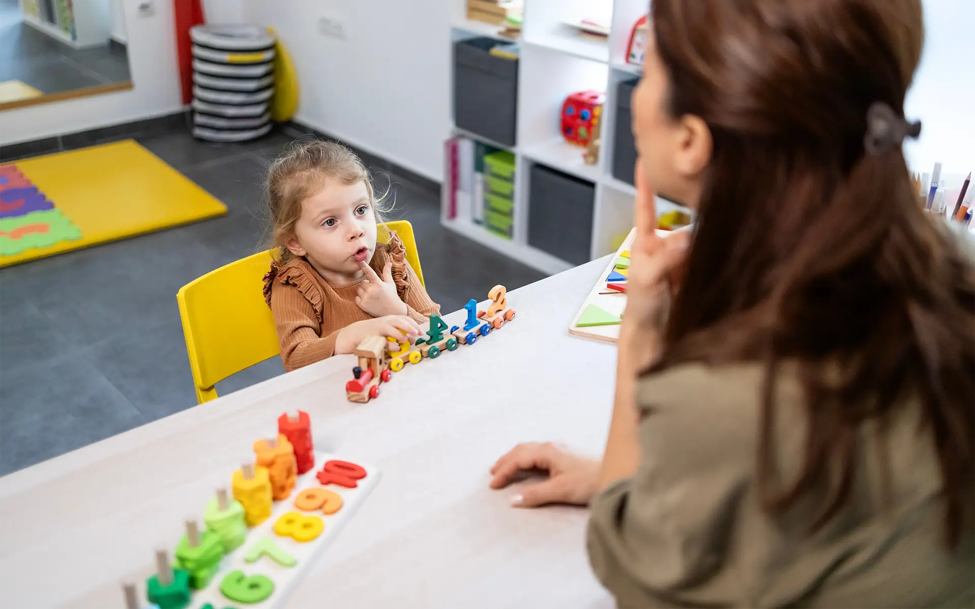 A speech therapist assists a young girl with speech development, engaging in language lessons and communication therapy using educational toys