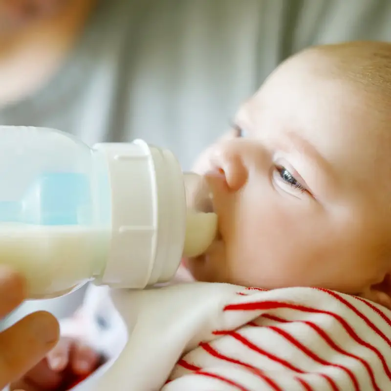 Close-up picture of an infant feeding from a bottle while being held in a parent's arms