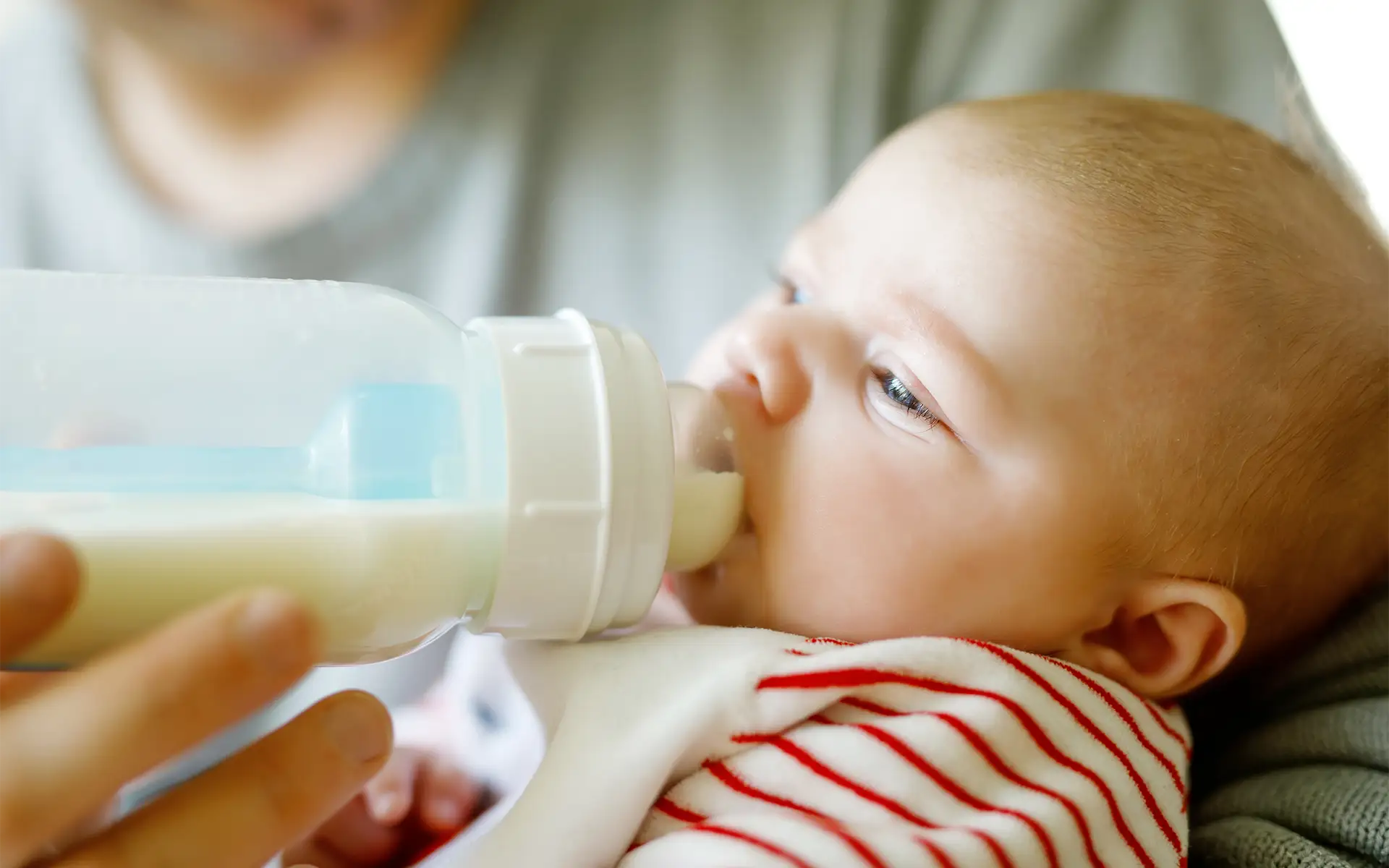 Close-up picture of an infant feeding from a bottle while being held in a parent's arms