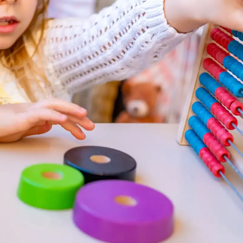 A young girl playing hand-eye coordination games with an abacus toy, grasping and moving blue and red beads