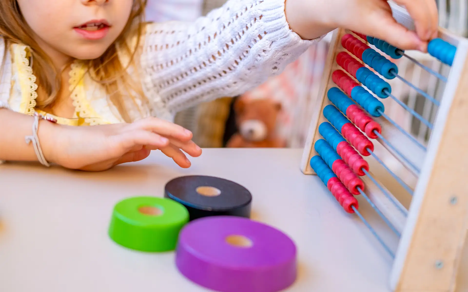 A young girl playing hand-eye coordination games with an abacus toy, grasping and moving blue and red beads